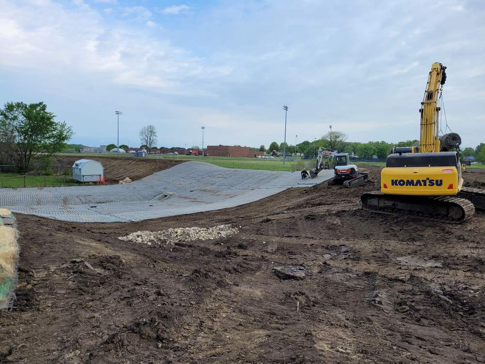 A detention basin shaped and graded, with turf reinforcement matting laid over the flow path and an outlet structure in place.