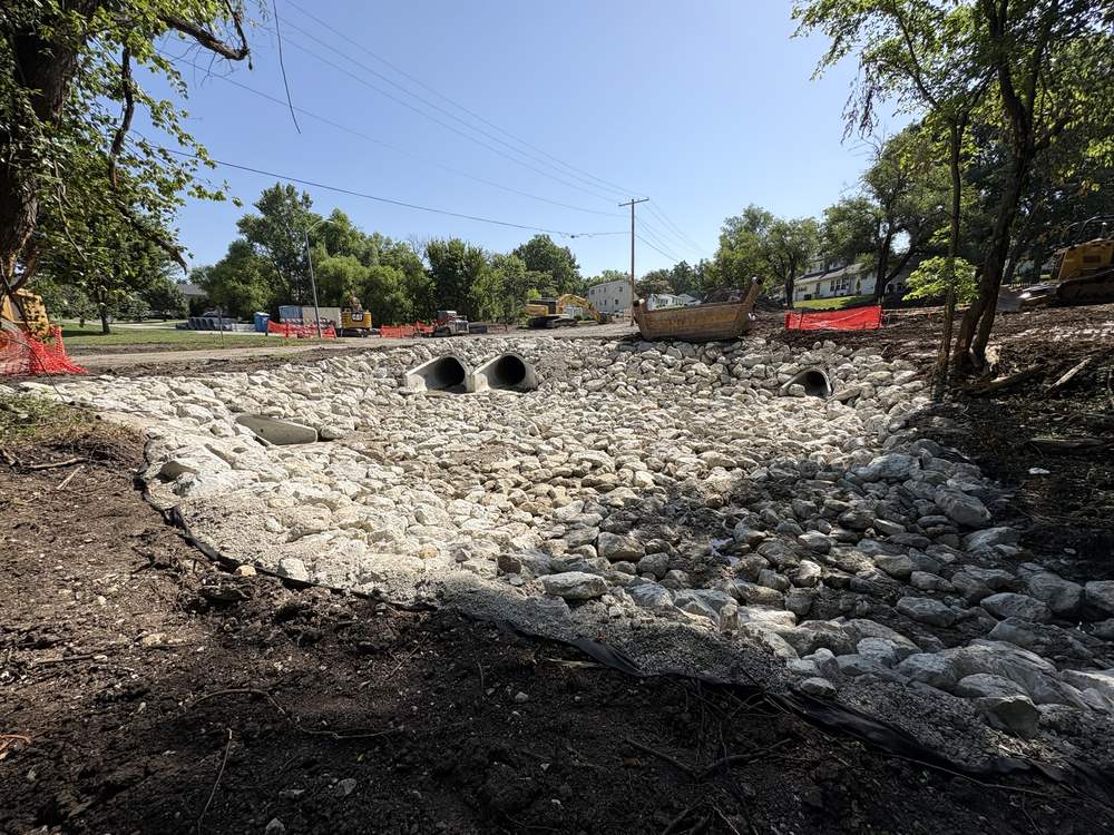 A completed twin culvert outlet discharging into a rock-lined channel with graded riprap and filter fabric at the edge.