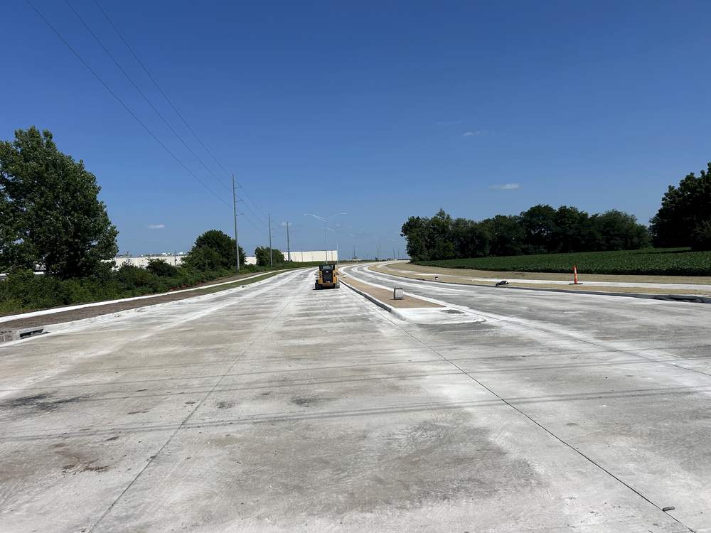 A newly placed concrete roadway with sawn joints, curb and a raised median, no traffic on it yet.