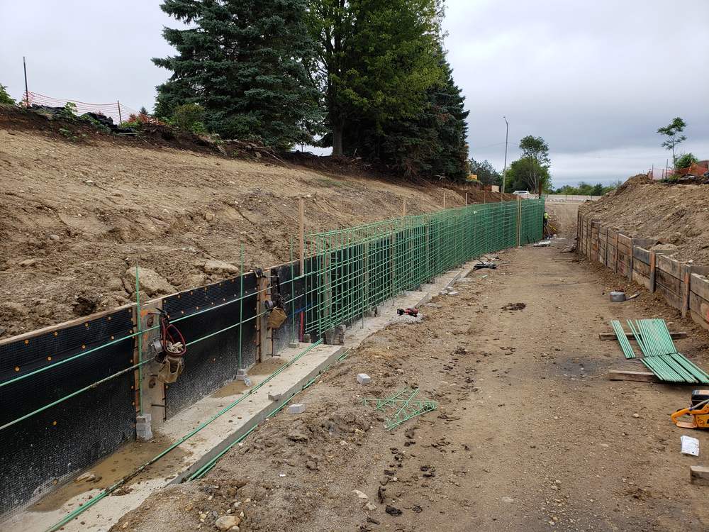 A cast-in-place concrete retaining wall under construction, with an epoxy coated reinforcing cage, drainage board against the back face and formwork braces.